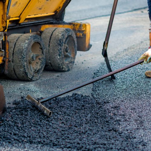 Worker regulate tracked paver laying asphalt heated to temperatures above 160 ° pavement on a runway