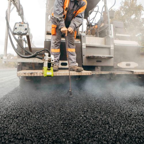Road service build the highway, road worker measures the depth of fresh asphalt